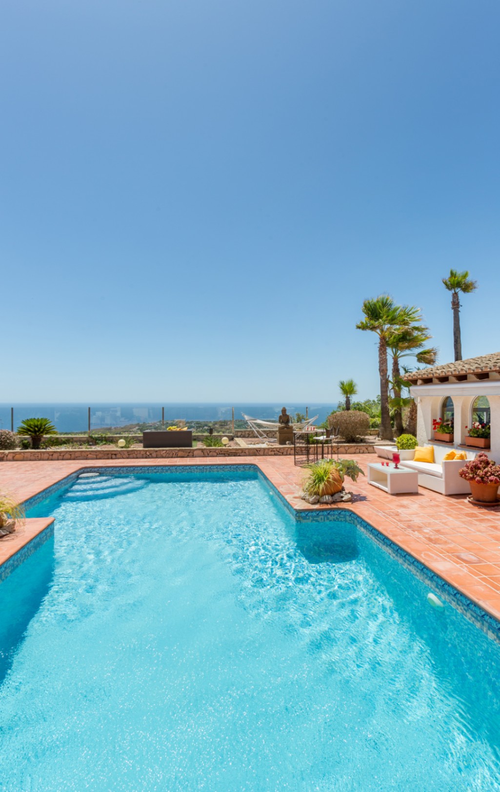 Swimming pool with blue mosaic tiles and terracotta terrace featuring a lounge area, palm trees, and panoramic Mediterranean Sea views.