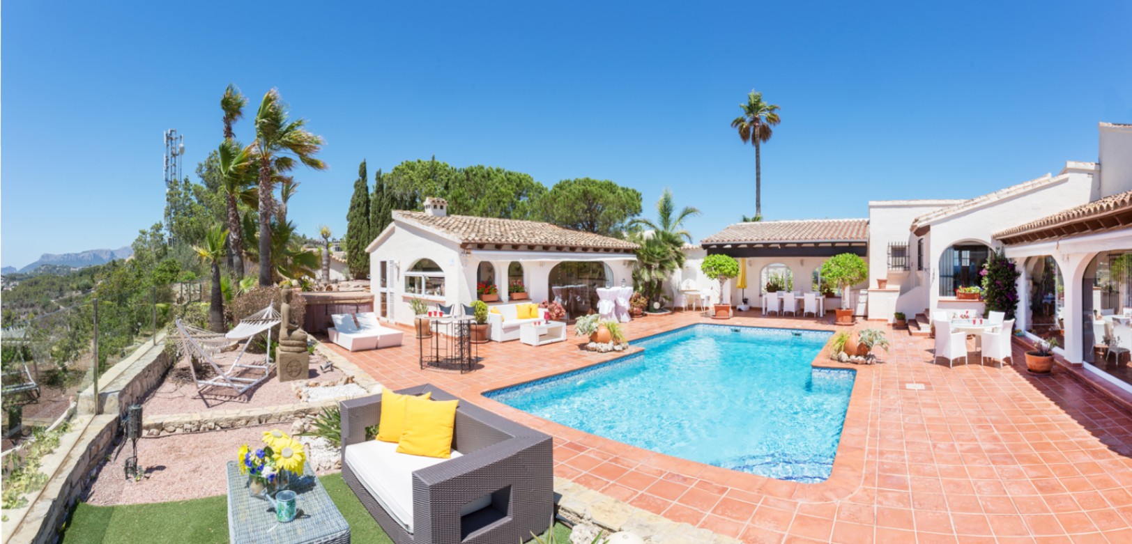 Terrace with a rectangular tiled swimming pool, terracotta flooring, and multiple lounge areas. The Mediterranean architecture features white walls and arched windows.