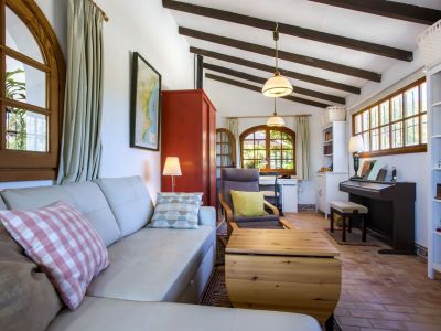 Bright living room with leather sofa, wood beams, and terracotta floors, combining living and work areas.