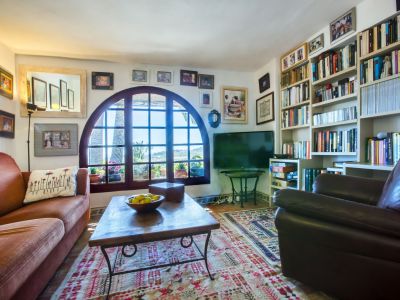 Living room with arched window and views, decorated with patterned carpet and a bookshelf full of books.