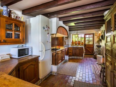 Rustic kitchen featuring terracotta floors, wood beams, and dark wood cabinetry. Natural light streams in through the glazed door.