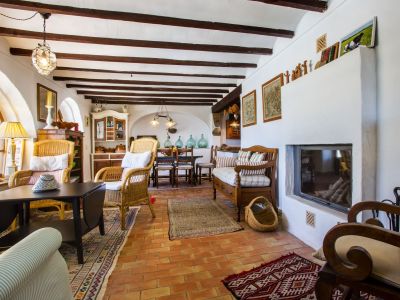Rustic living room featuring a masonry fireplace, exposed wood beams, and terracotta flooring. Traditional decor and wicker furniture.