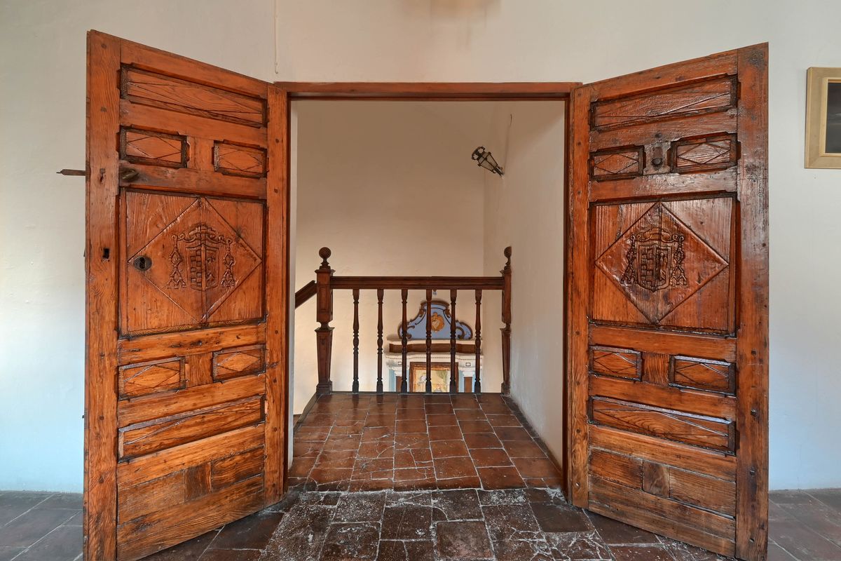 Antique double wooden doors with hand-carved heraldic shields lead to a landing with traditional terracotta tiles and a classic balustrade.