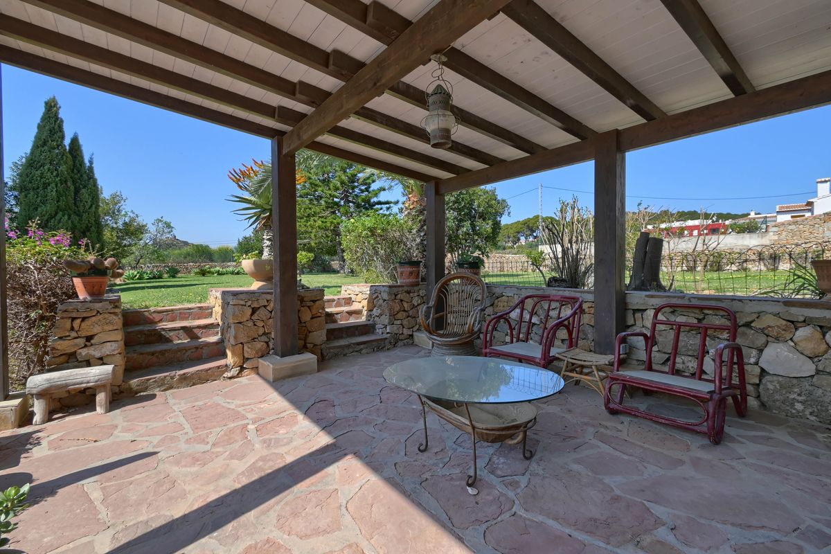 Covered terrace featuring exposed wooden beams, natural stone flagstone flooring, and rustic stone walls overlooking the expansive green garden.