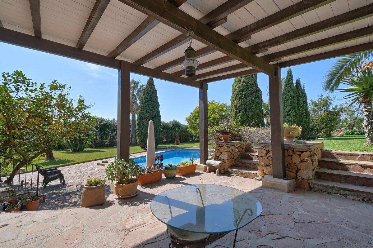 Covered terrace featuring wooden beams and stone flooring, overlooking the private swimming pool and landscaped gardens.