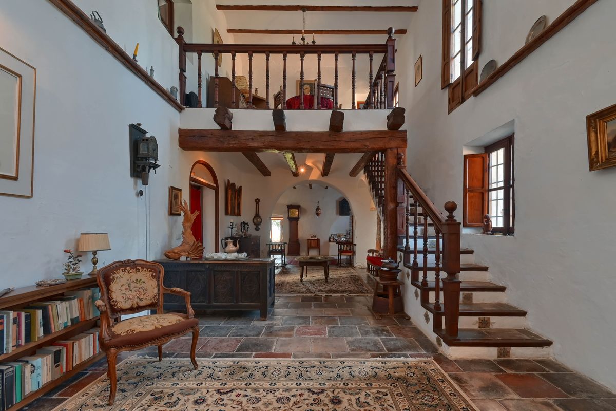 Double-height living area featuring exposed timber beams, rustic stone flooring, and a mezzanine gallery overlooking the traditional interior.