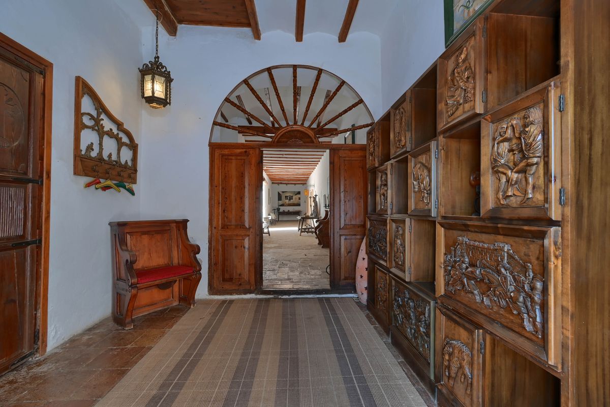 Entrance hall featuring ornate wood-carved cabinets, exposed ceiling beams, and a traditional arched doorway leading to a stone-paved corridor.