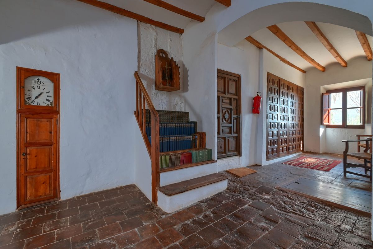 Hallway featuring terracotta tiles, exposed beams, and a built-in grandfather clock. A small staircase with integrated bookshelves sits beside traditional wooden doors.