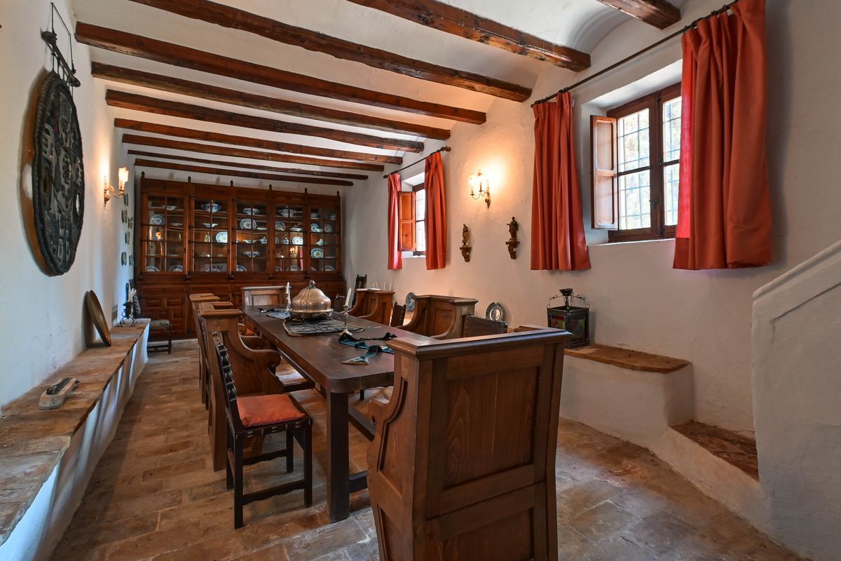 Historic dining room featuring exposed wooden ceiling beams, terracotta flooring, and a large built-in wooden display cabinet with ceramics.