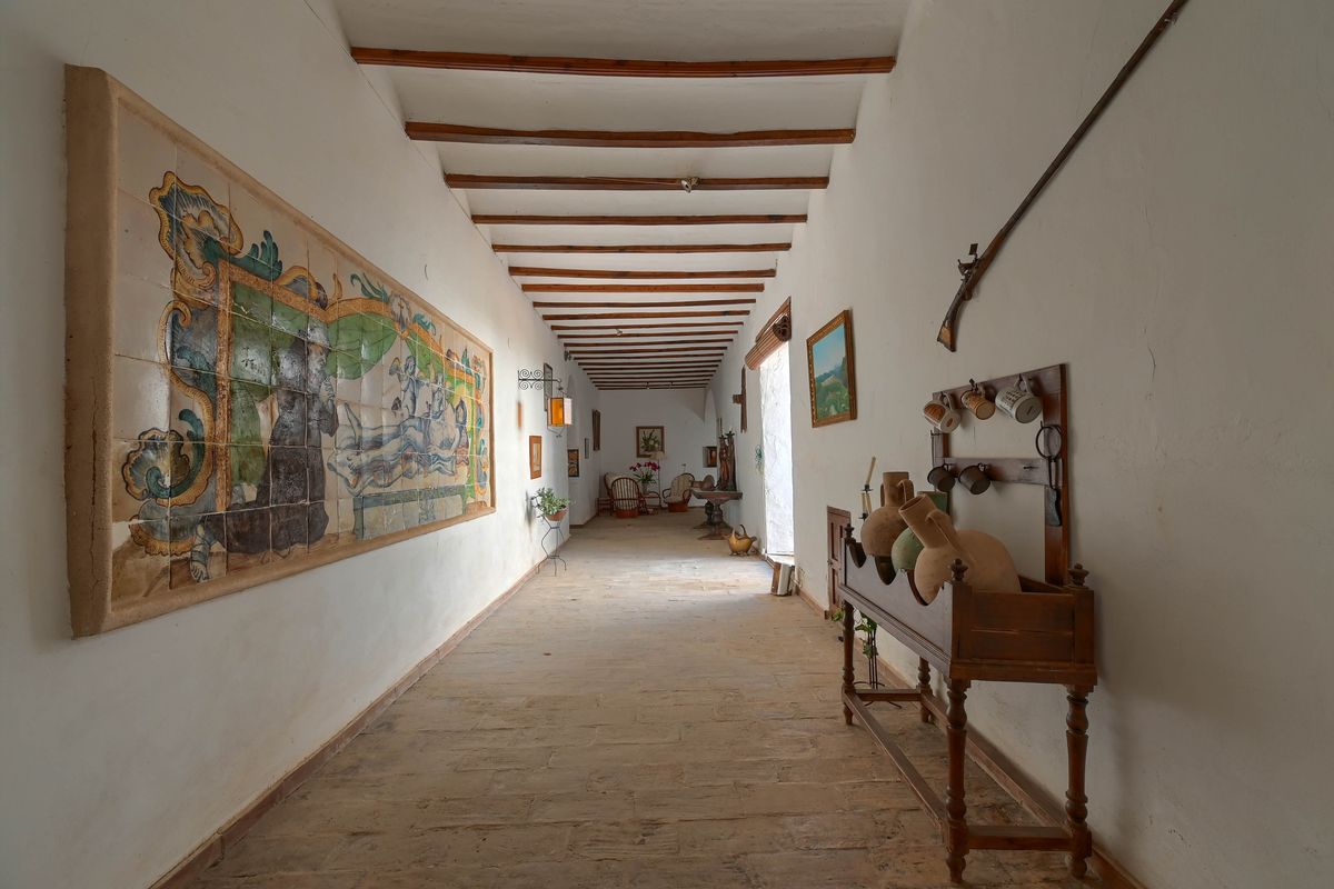 Historic hallway featuring exposed wooden ceiling beams, natural stone flooring, and a large hand-painted ceramic tile mural.
