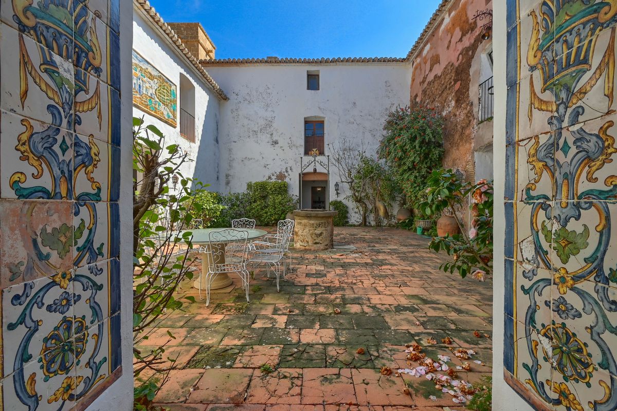 Historic interior courtyard featuring terracotta tile flooring, a central stone well, and decorative ceramic tile murals on the entrance pillars.