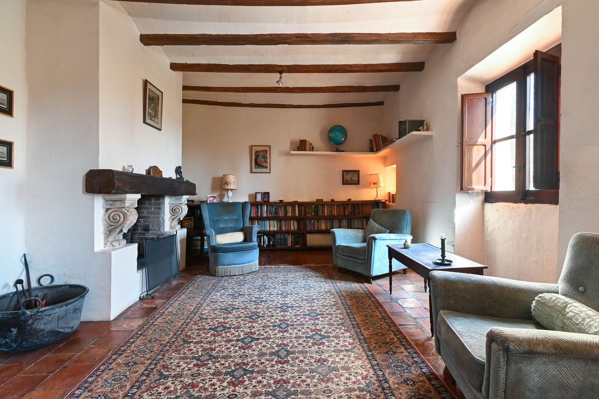 Historic living area featuring exposed wooden ceiling beams, a large fireplace with a timber mantle, and traditional terracotta floors.