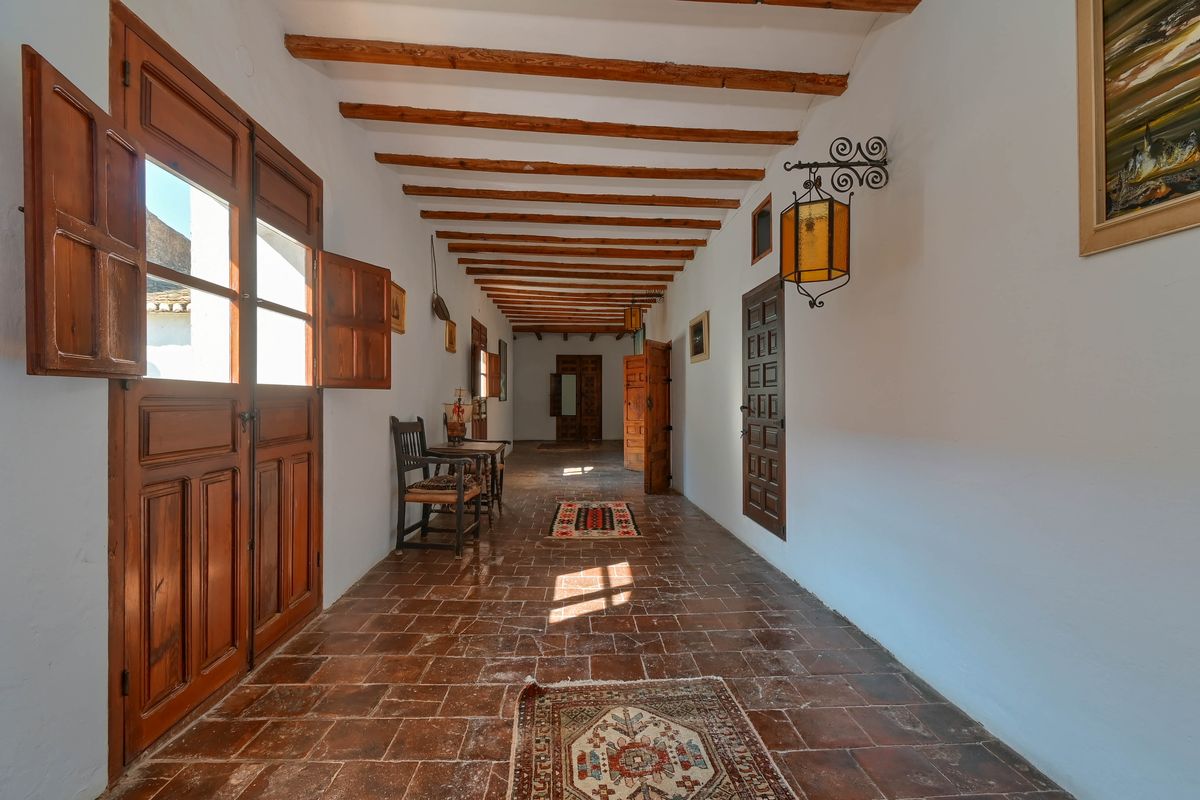 Long corridor featuring exposed wooden ceiling beams, authentic terracotta tile flooring, and traditional solid wood doors with shutters.