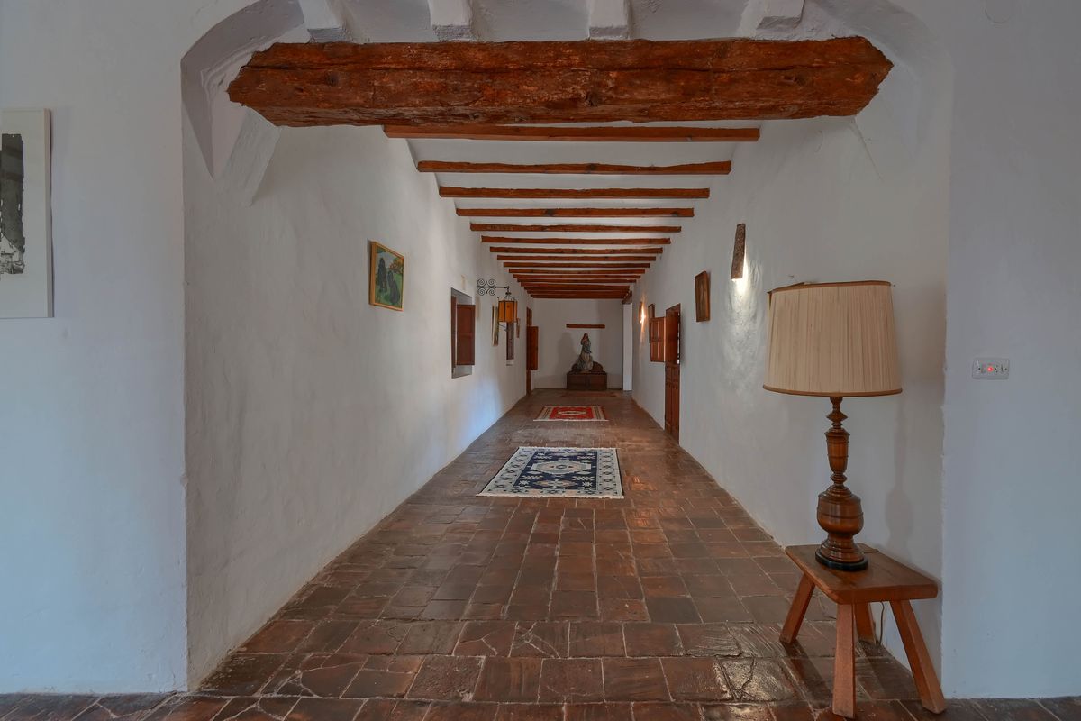 Long hallway featuring authentic terracotta floor tiles, thick whitewashed walls, and a ceiling with exposed heavy timber beams.