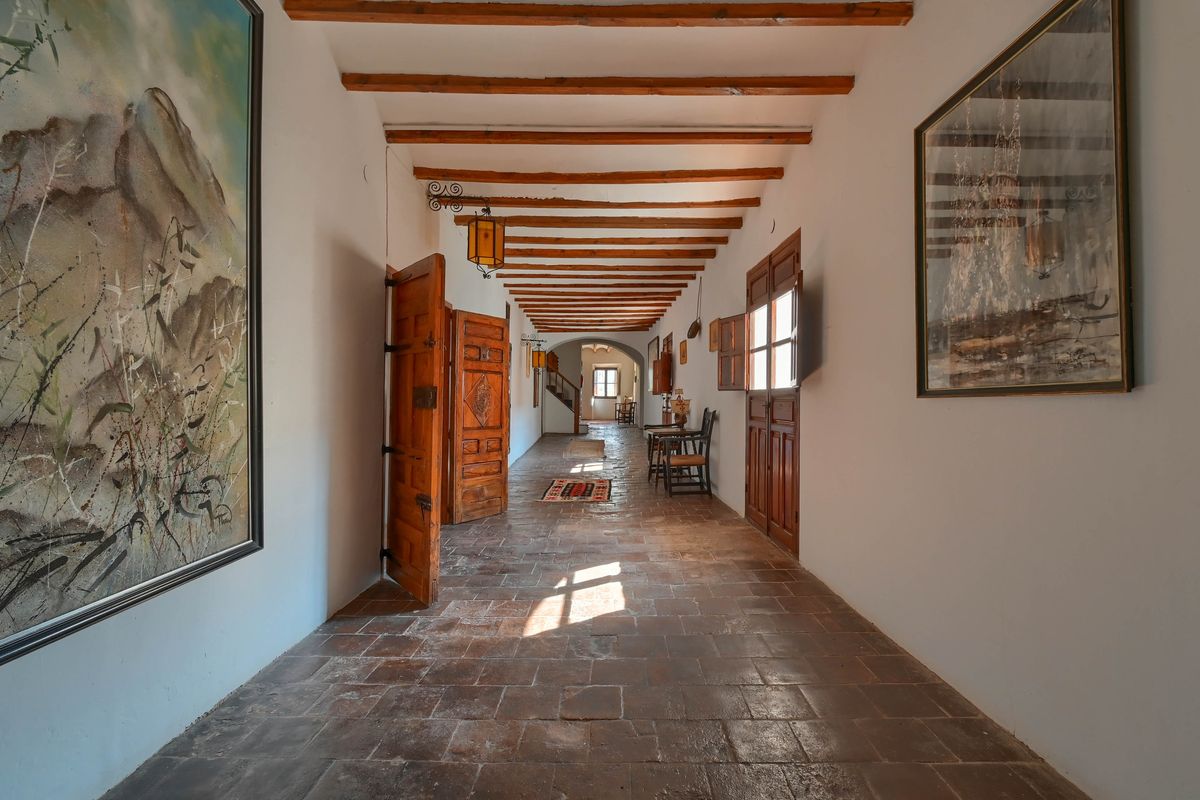 Long hallway featuring traditional terracotta tile flooring, exposed wooden ceiling beams, and heavy carved wooden doors with natural light.