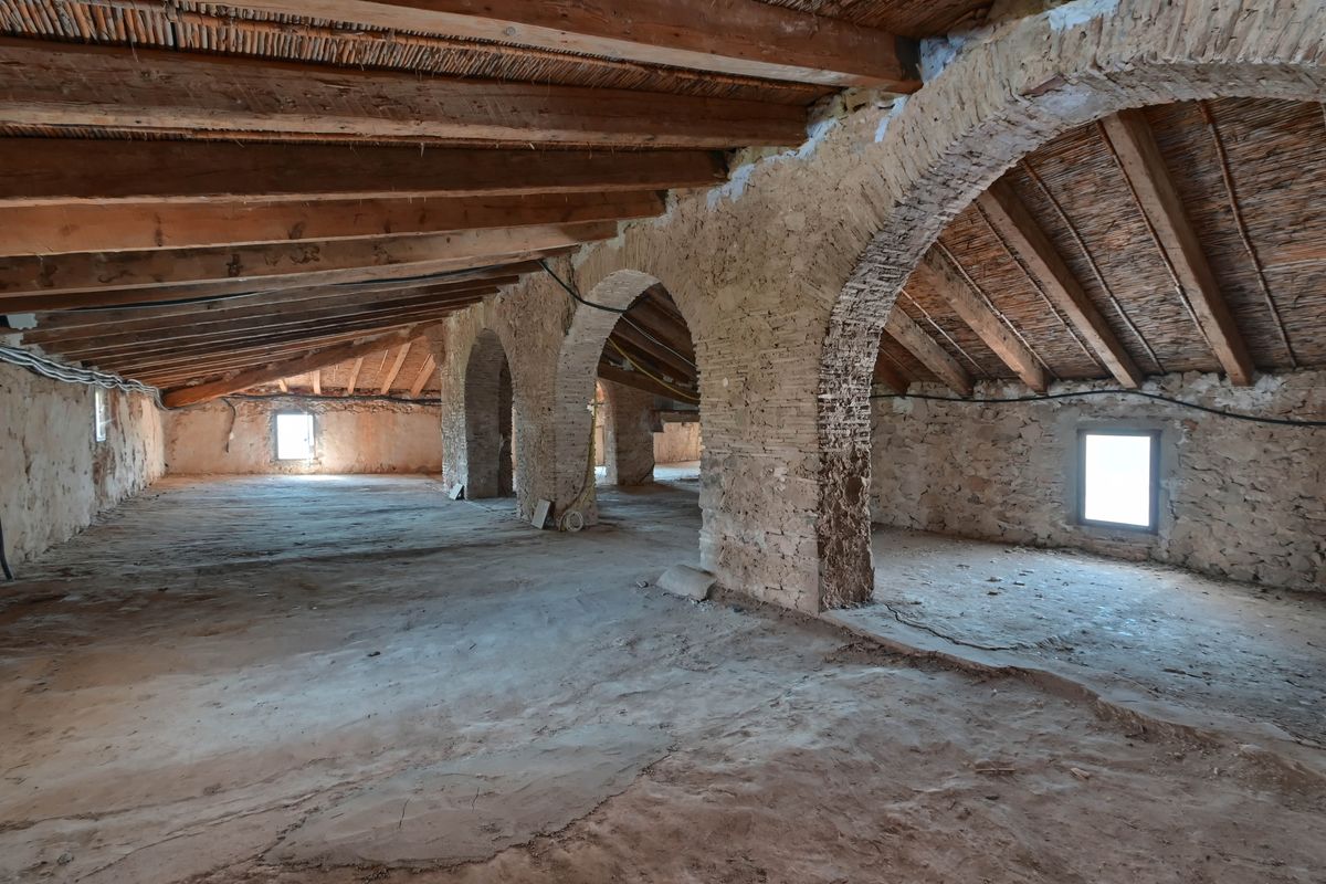 Open attic space featuring original wooden beams, traditional cane ceilings, and structural stone and brick arches awaiting restoration.