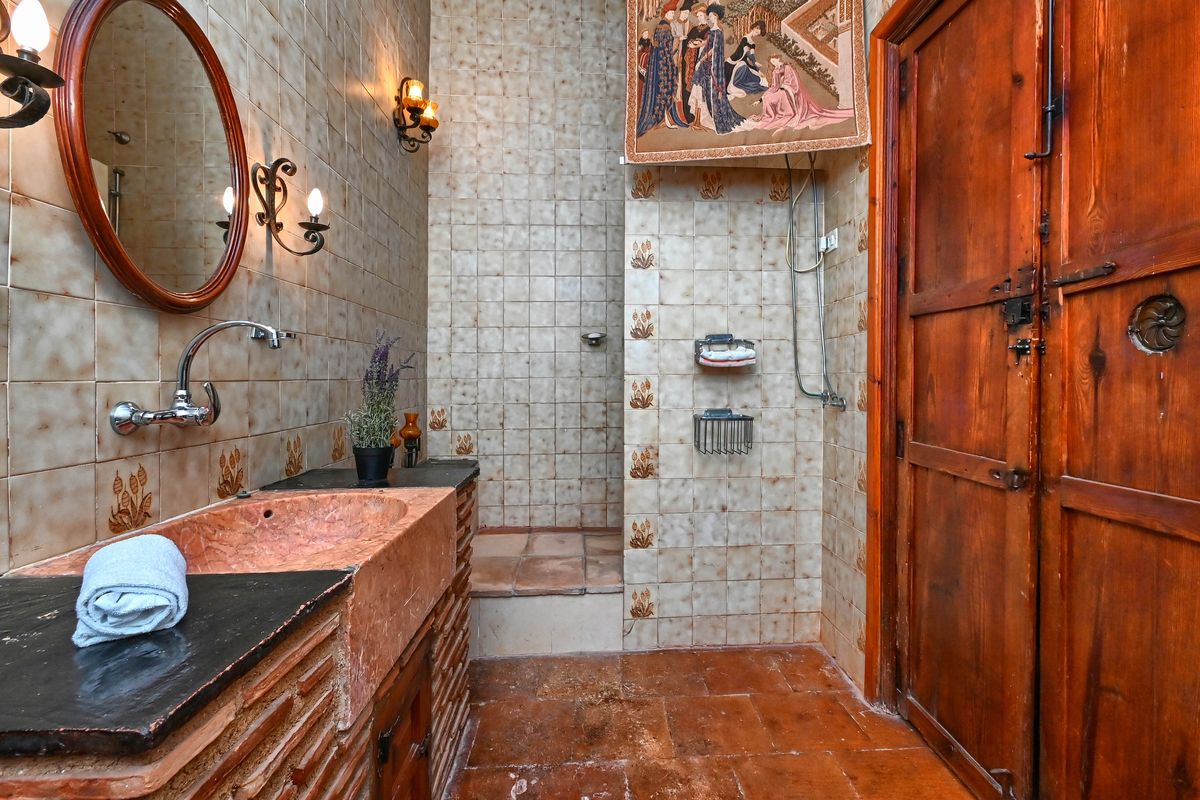 Rustic bathroom featuring a pink stone basin, decorative ceramic wall tiles, wrought iron sconces, and a traditional solid wood door.