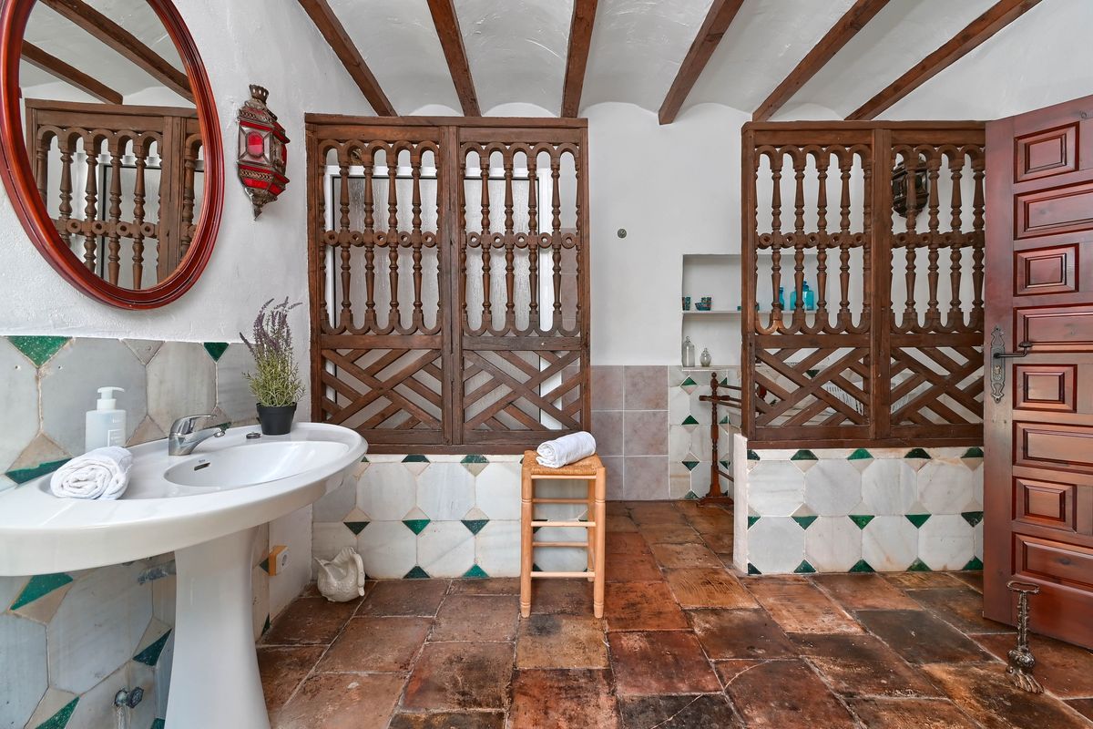 Rustic bathroom featuring exposed ceiling beams, terracotta flooring, a pedestal sink, and intricate carved wooden screens.
