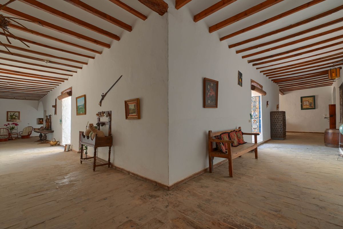 Spacious hallway featuring traditional exposed wooden beams, rustic stone flooring, and white-washed walls decorated with antique furniture and historical artifacts.