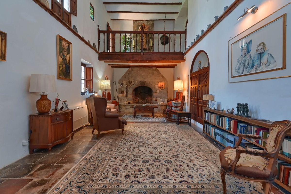 Spacious living room featuring a large stone fireplace, exposed wooden beams, and an upper wooden gallery overlooking the seating area with traditional tile flooring.