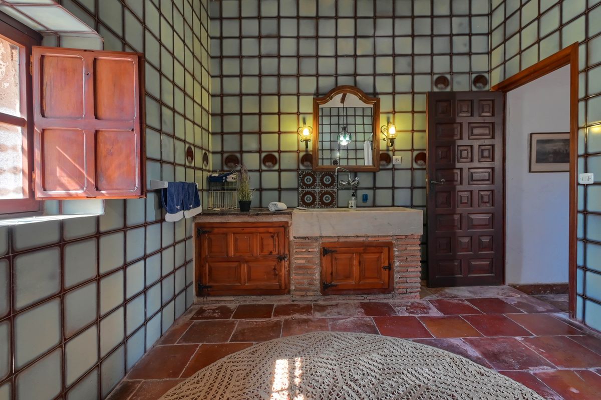 Traditional bathroom featuring a stone basin on a brick base, rustic wooden cabinetry, terracotta flooring, and distinctive grid-patterned wall tiling.