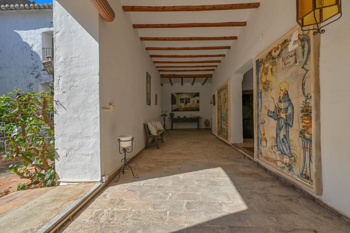 Traditional covered porch featuring exposed wooden beams, natural stone flooring, and a large historic religious ceramic tile mural on the side wall.