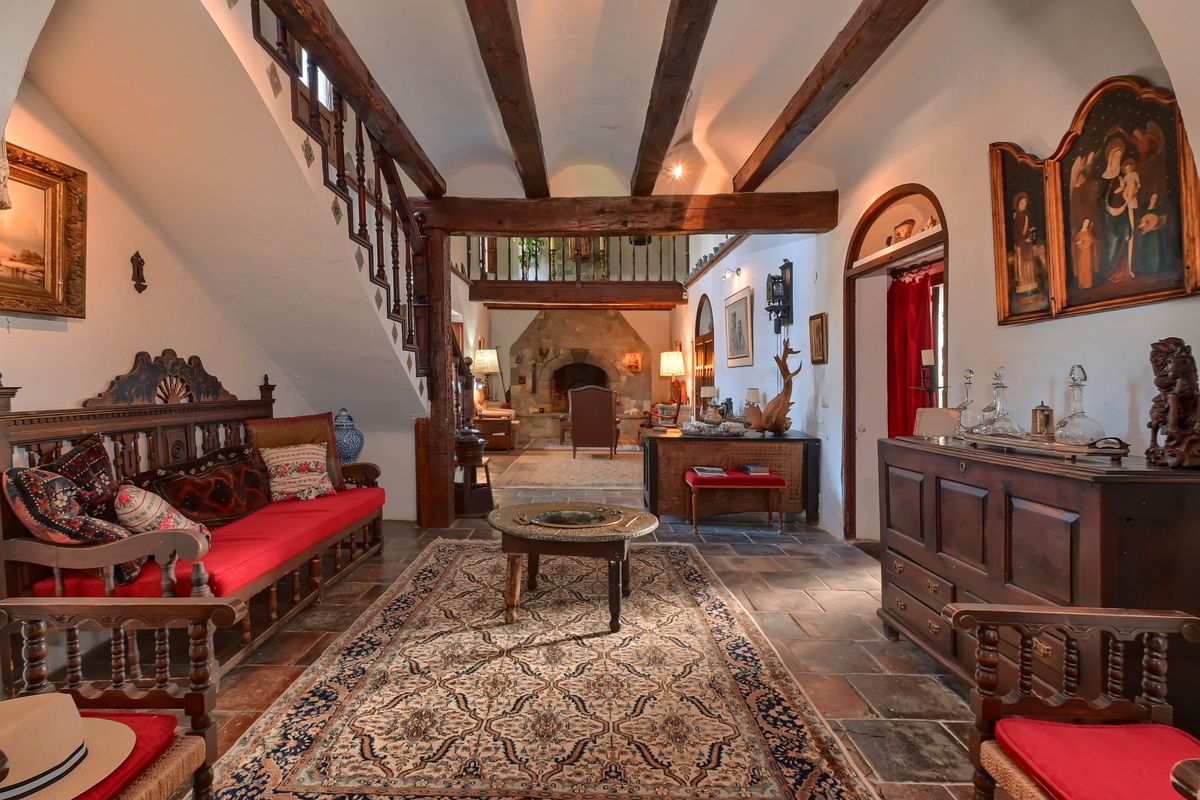 Traditional hall with exposed wooden beams, terracotta tile flooring, and a mezzanine. Features include carved wooden furniture and a stone fireplace.