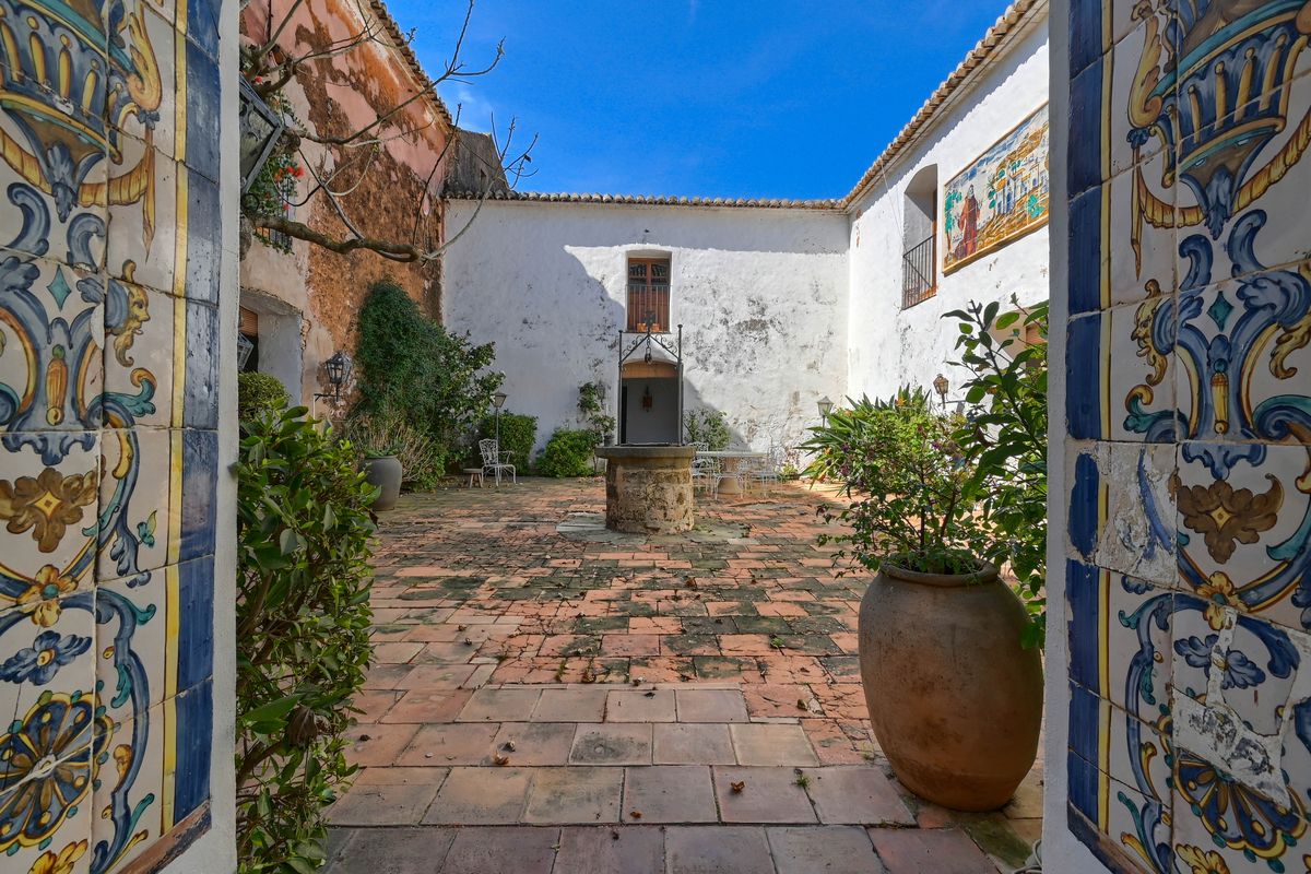 Traditional inner courtyard featuring a central stone well, terracotta tile flooring, and decorative hand-painted ceramic tiles on the entrance arch.