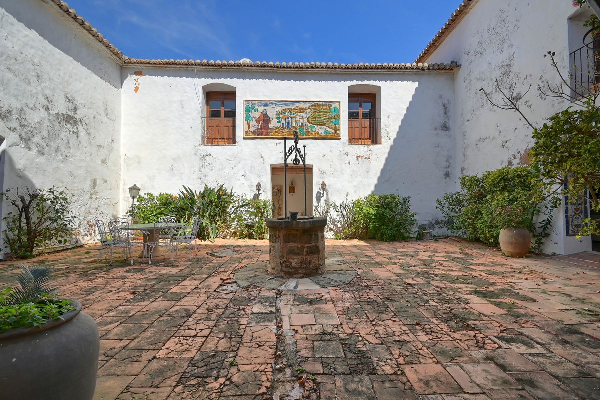 Traditional interior courtyard featuring rustic terracotta tiling, a central stone well with ironwork, and a large hand-painted ceramic mural.