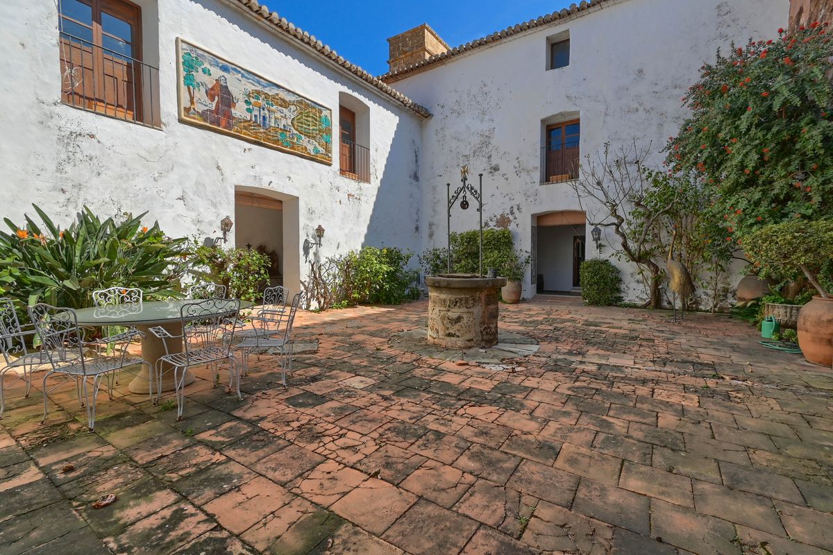 Traditional interior courtyard featuring terracotta tile flooring, a central stone well, and a decorative ceramic mural on authentic whitewashed walls.