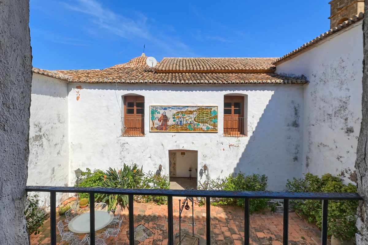 Traditional interior courtyard featuring terracotta tiling, a decorative ceramic tile mural, and white-washed walls under a clear sky.
