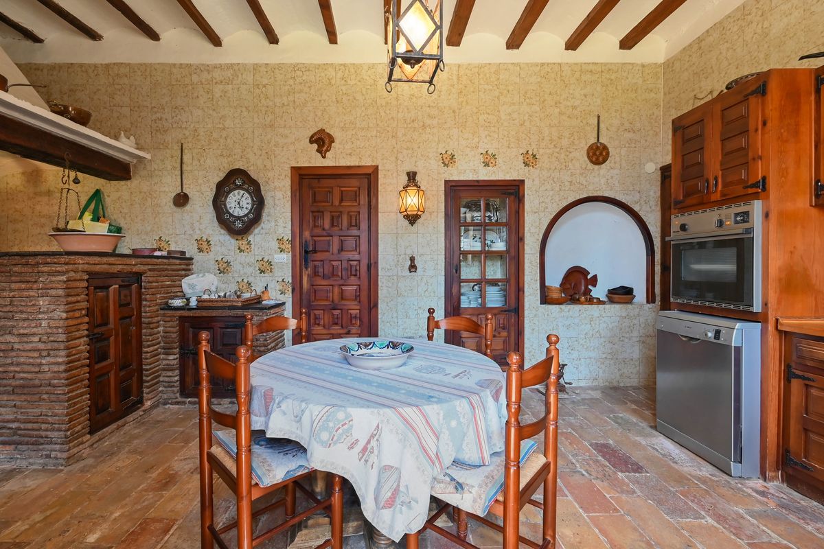 Traditional rustic kitchen featuring exposed ceiling beams, terracotta floors, and a brick hearth. Includes patterned wall tiles and integrated modern appliances.