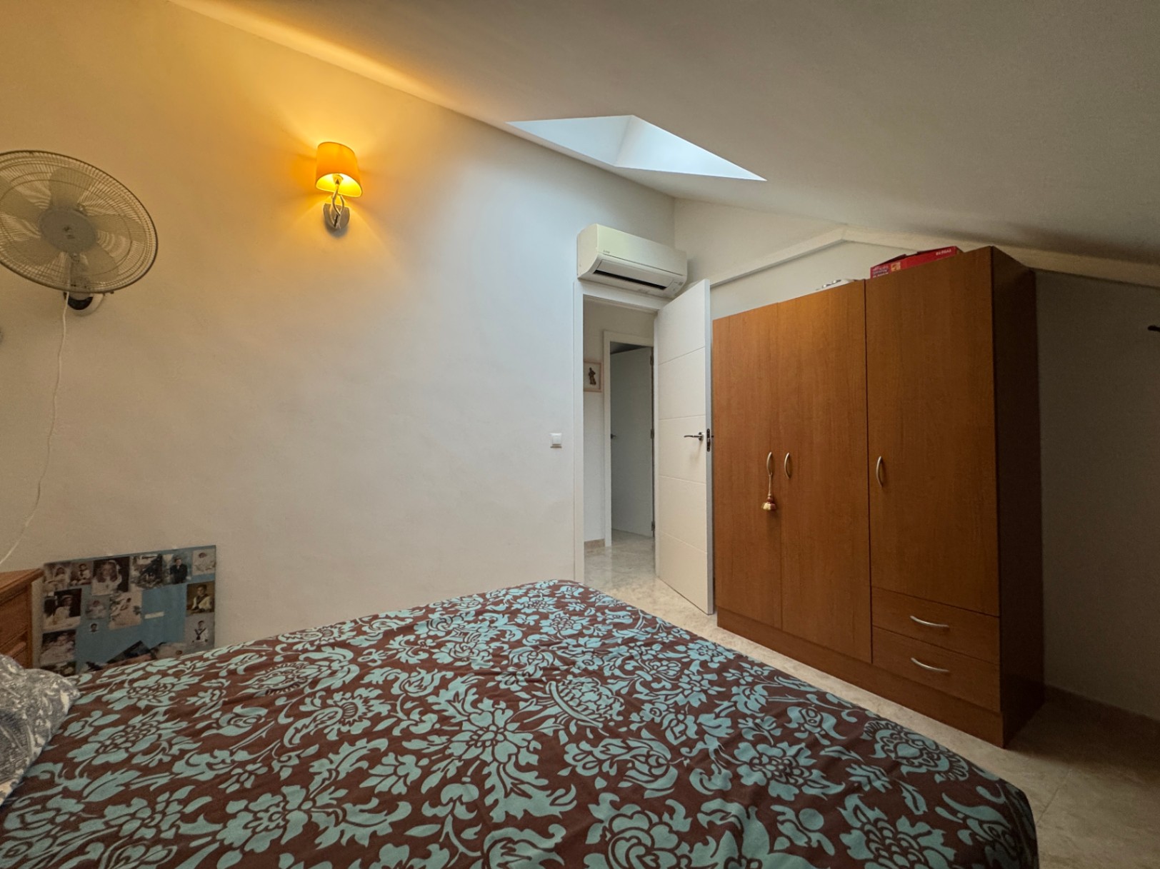 Bedroom featuring a patterned bedspread, wooden wardrobe, and warm ambient lighting.