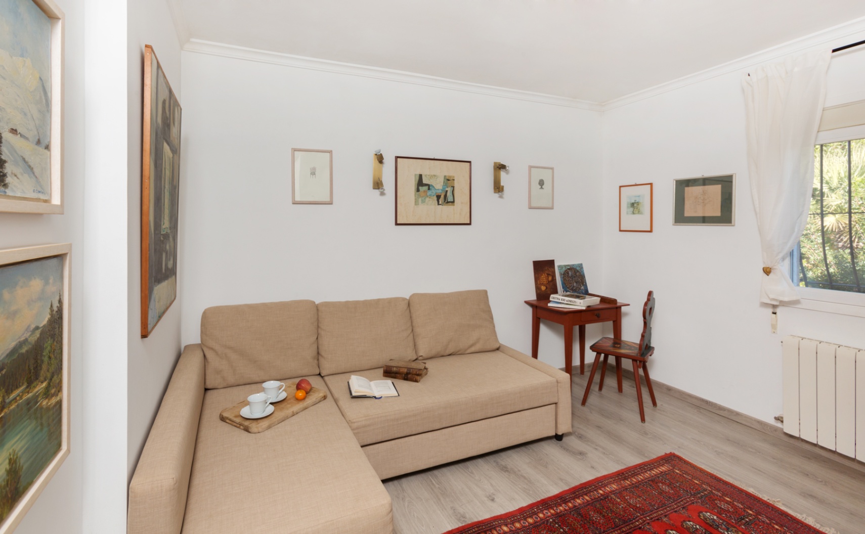 Bright sitting area featuring a beige chaise longue sofa, a classic wooden writing desk, and a gallery wall of framed art over light grey flooring.