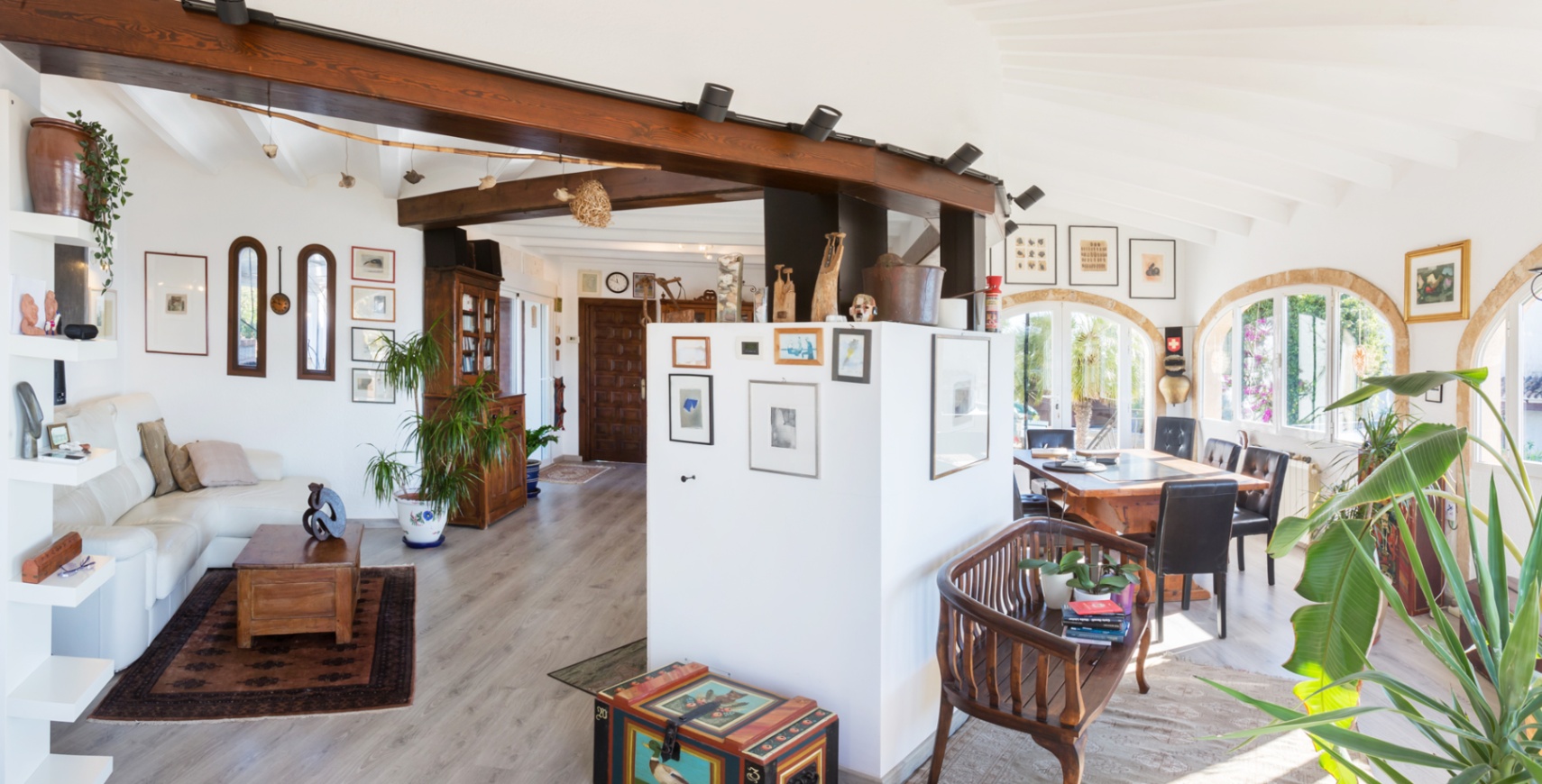 Open-plan living space featuring exposed dark wood beams, a vaulted ceiling, and arched windows that provide abundant natural light to the dining and lounge areas.