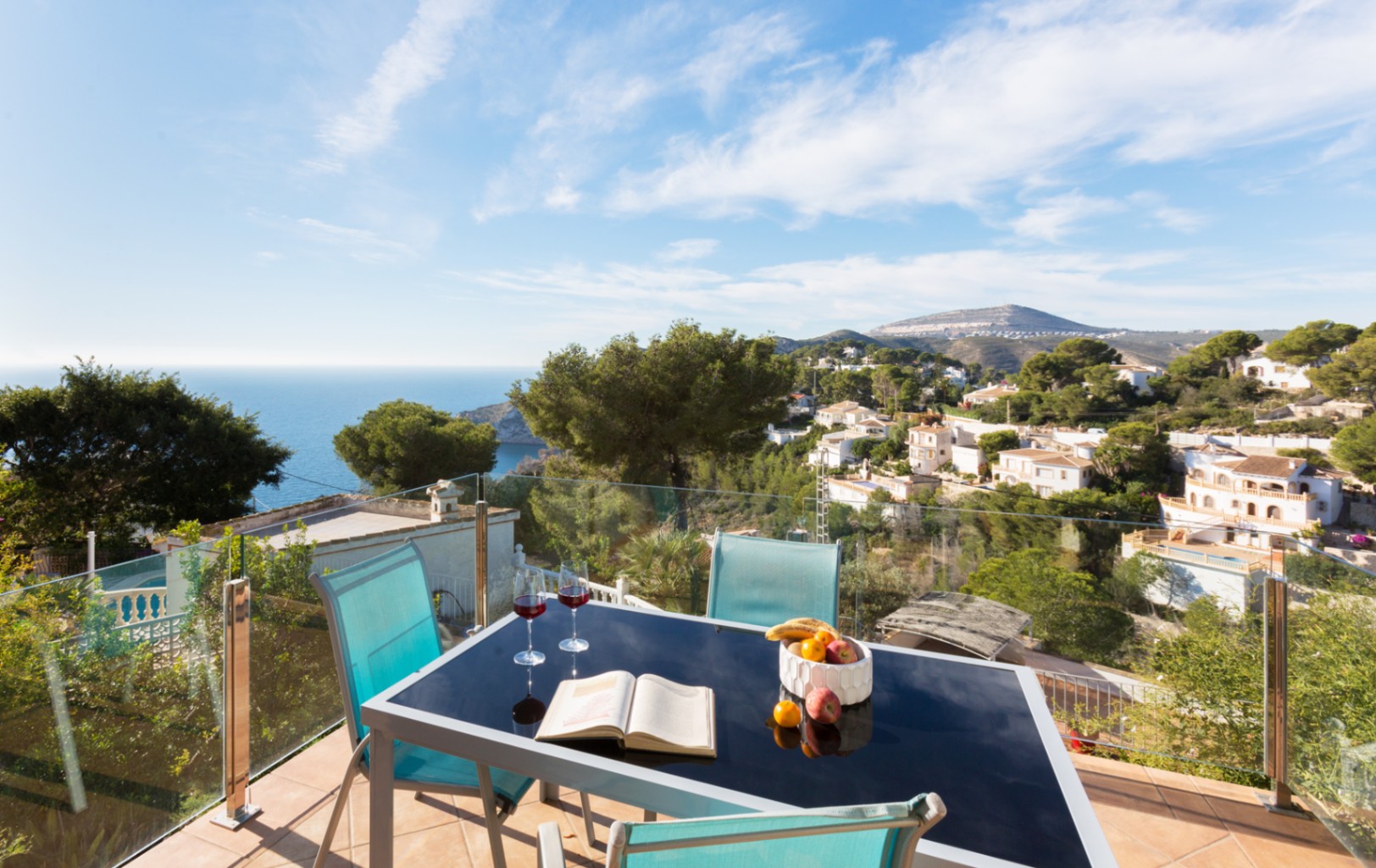 Terrace with glass railing featuring a black dining table and panoramic views of the Mediterranean coast and surrounding hills in Cumbre del Sol.