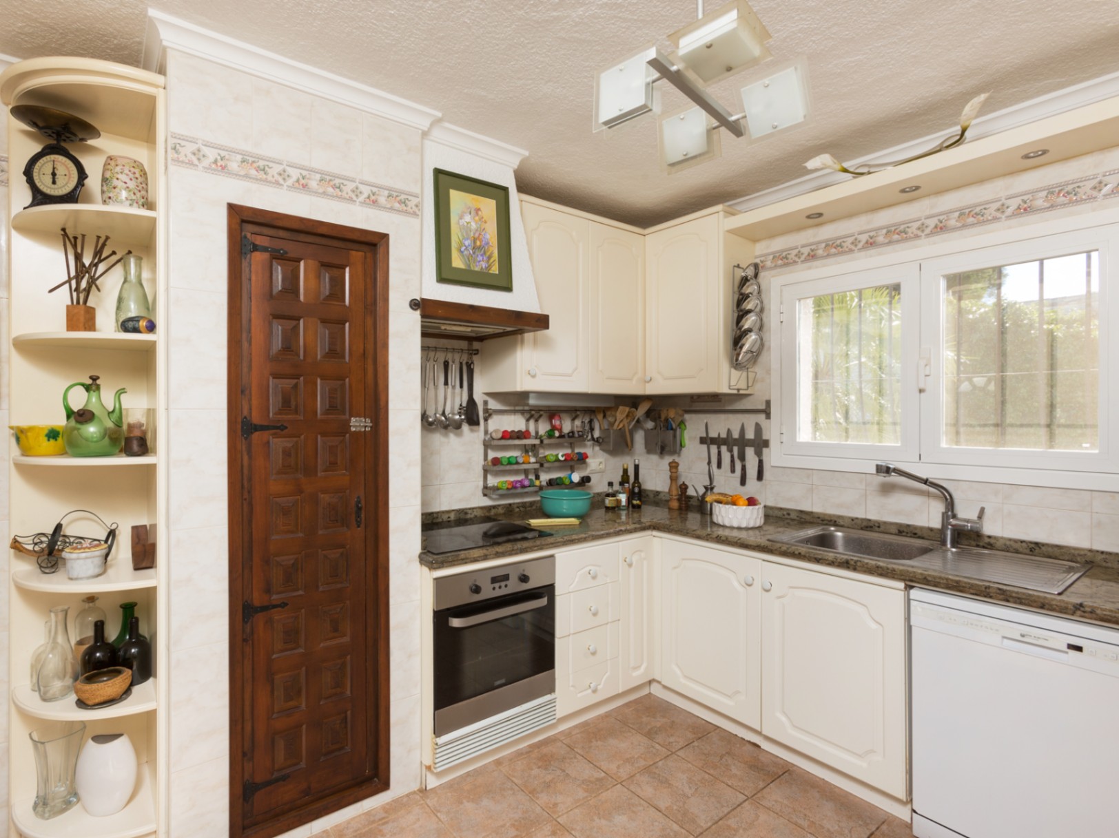 Traditional kitchen featuring cream cabinetry, granite countertops, and a decorative dark wood pantry door. Includes integrated appliances and a window overlooking the garden.