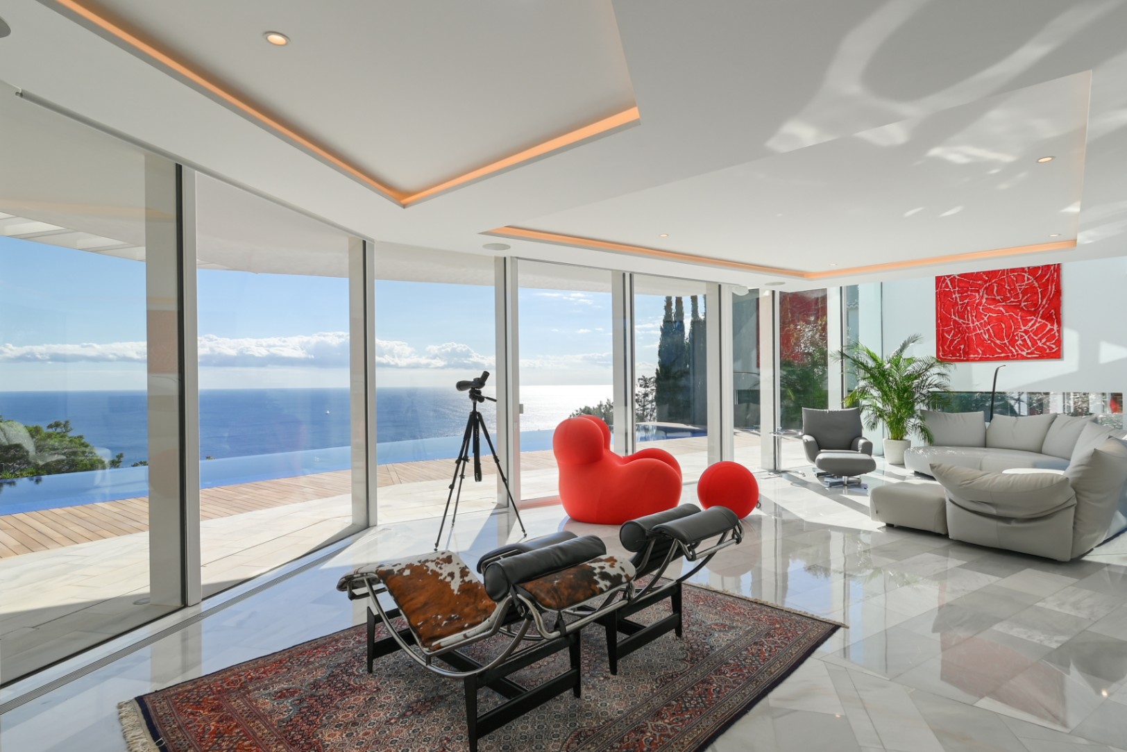 Bright lounge featuring floor-to-ceiling glass, marble flooring, and designer seating with panoramic views of the infinity pool and sea.