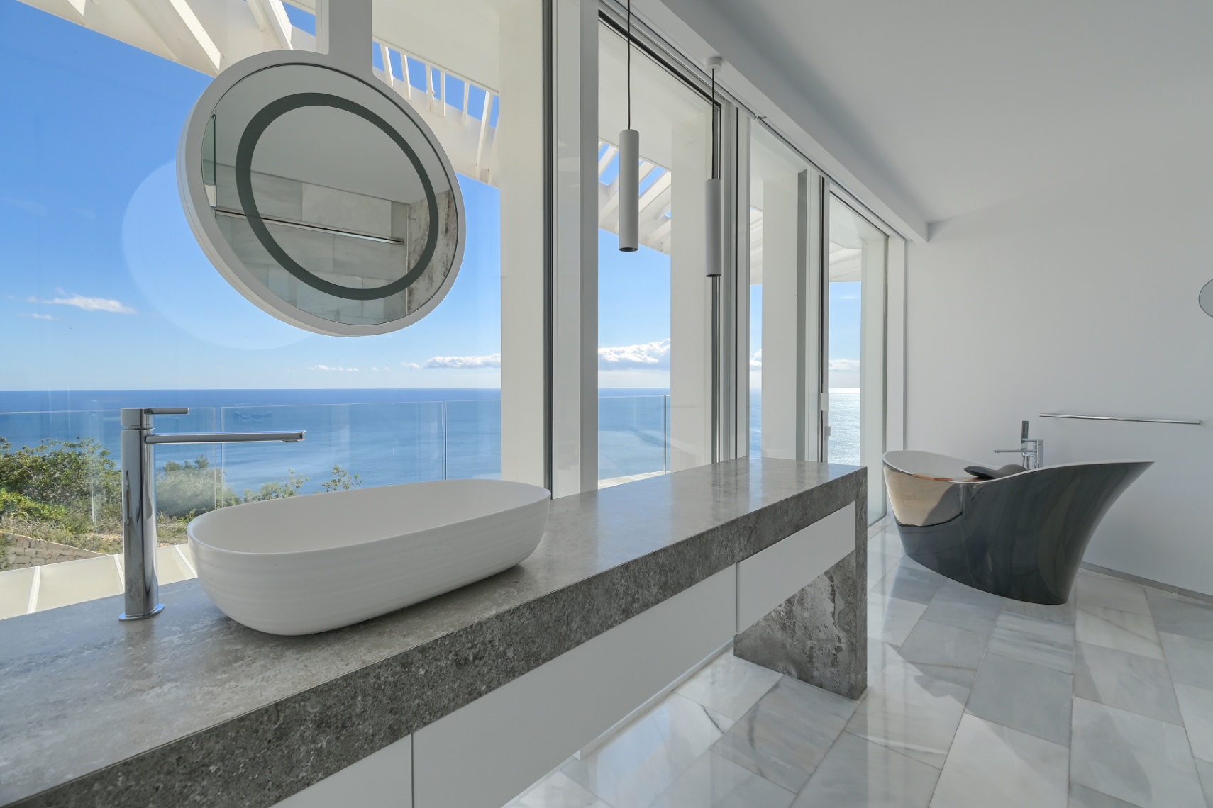 Modern bathroom featuring a grey stone vanity with a vessel sink, a sculptural freestanding bathtub, and floor-to-ceiling windows with panoramic sea views.