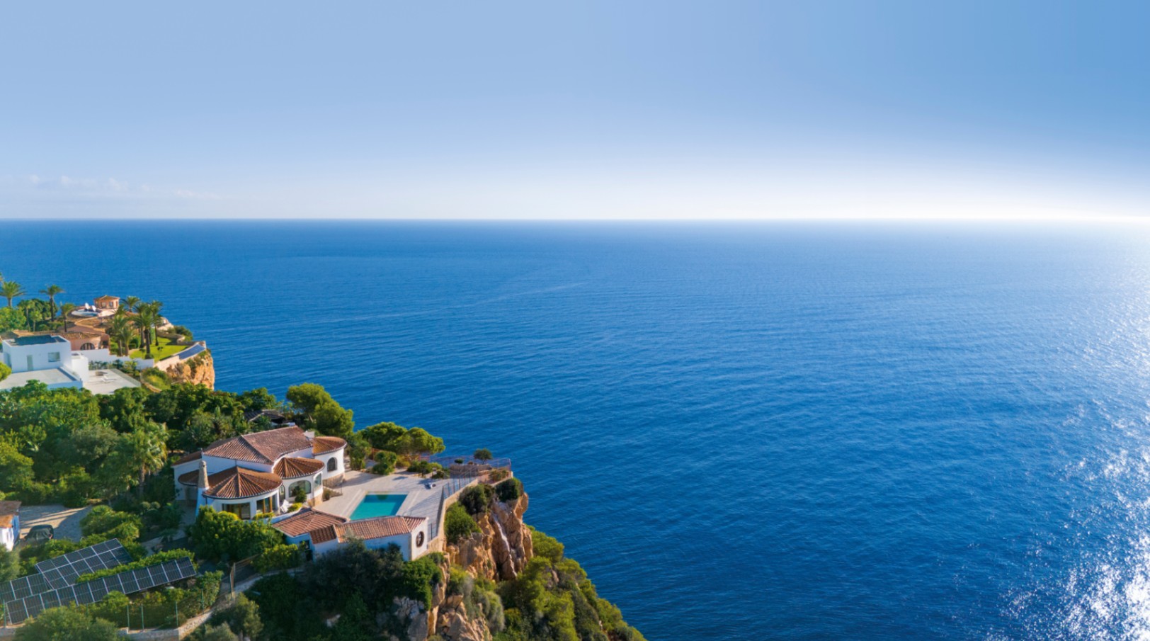 Aerial view of a cliffside villa featuring terracotta roofs, a private terrace with a pool, and expansive views of the blue Mediterranean Sea.