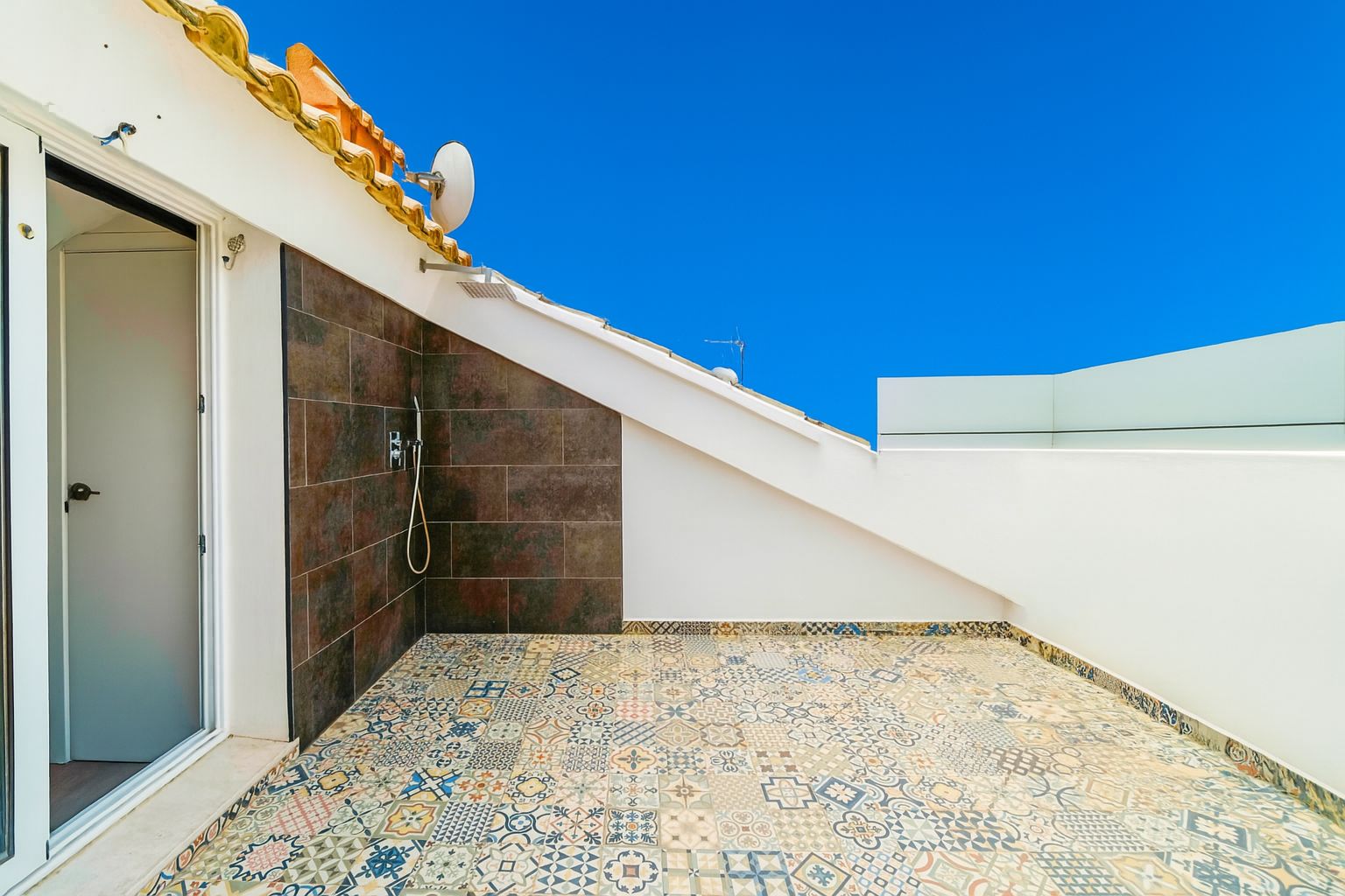 Rooftop terrace featuring patterned floor tiles, an outdoor shower with dark ceramic tiling, and a modern glass balustrade.