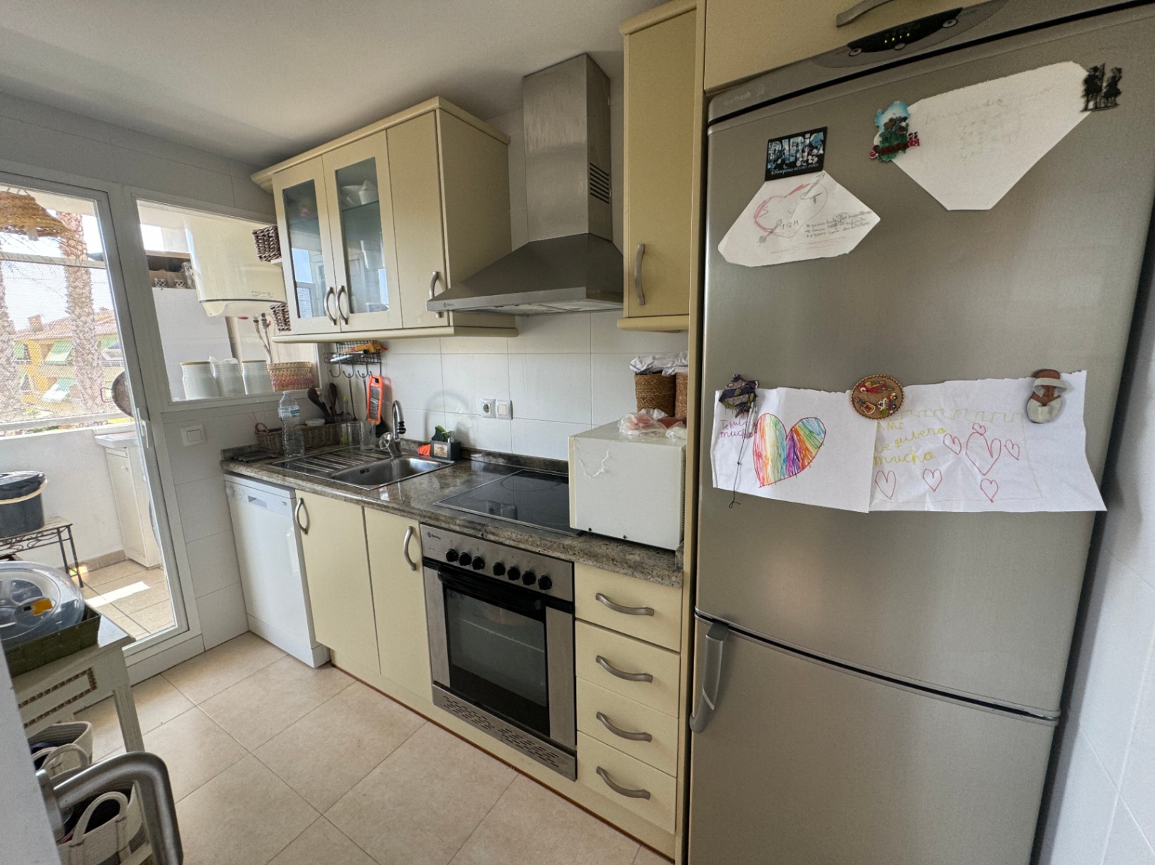 Functional kitchen featuring cream cabinetry, granite countertops, and stainless steel appliances. Includes an integrated oven, extractor hood, and access to an outdoor terrace.