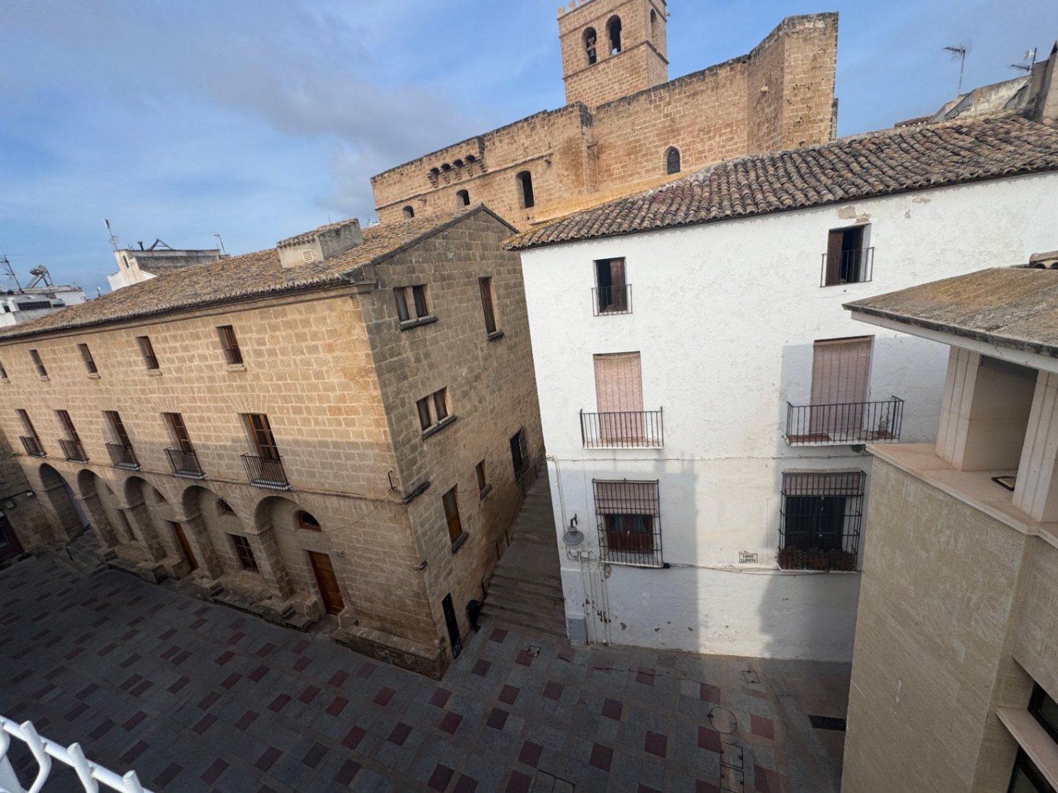 Elevated view of a traditional town square featuring stone masonry architecture, arched entryways, and a historic bell tower in the background.