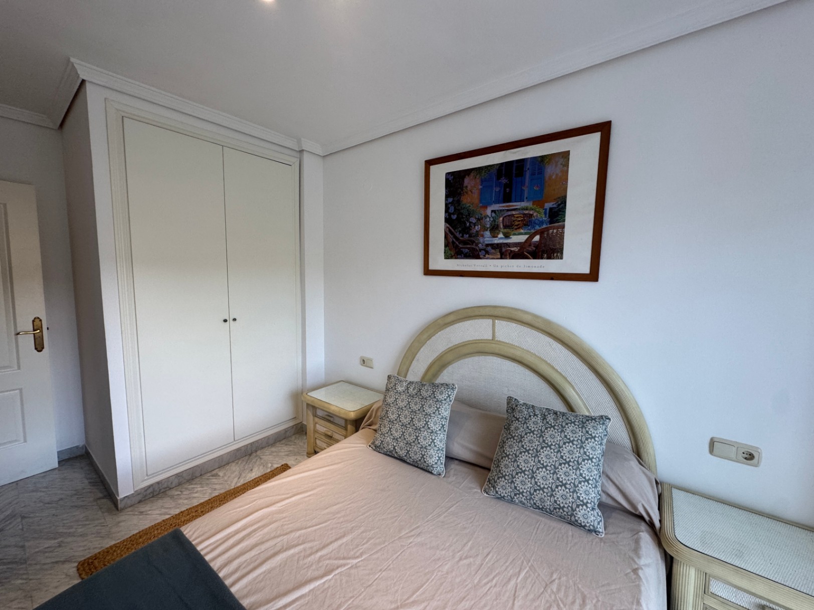 Bedroom featuring a built-in white wardrobe, marble flooring, and a bed with a curved headboard flanked by matching bedside tables.