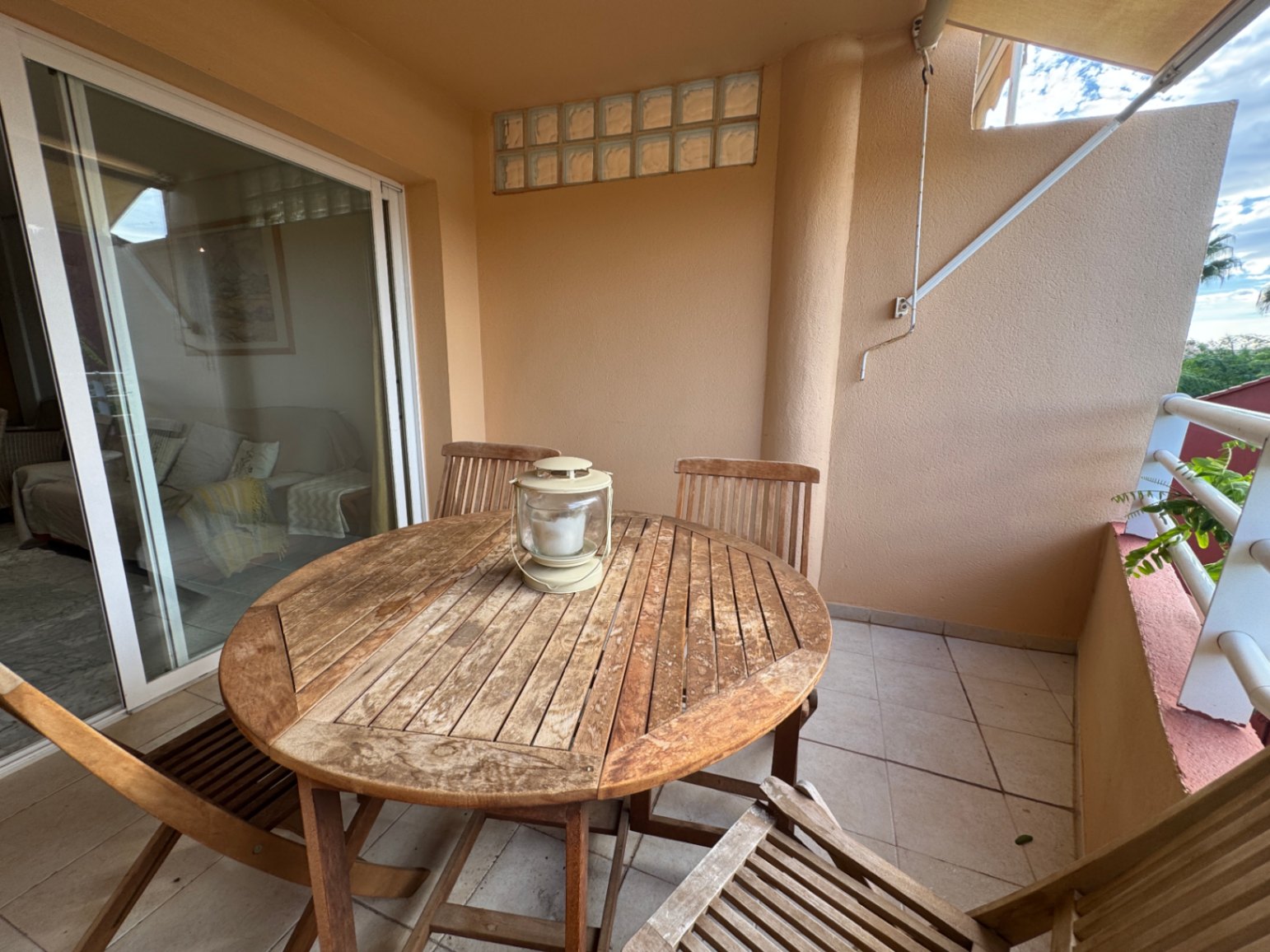 Covered terrace featuring a round wooden dining set and tiled flooring, accessible via large sliding glass doors from the living area.