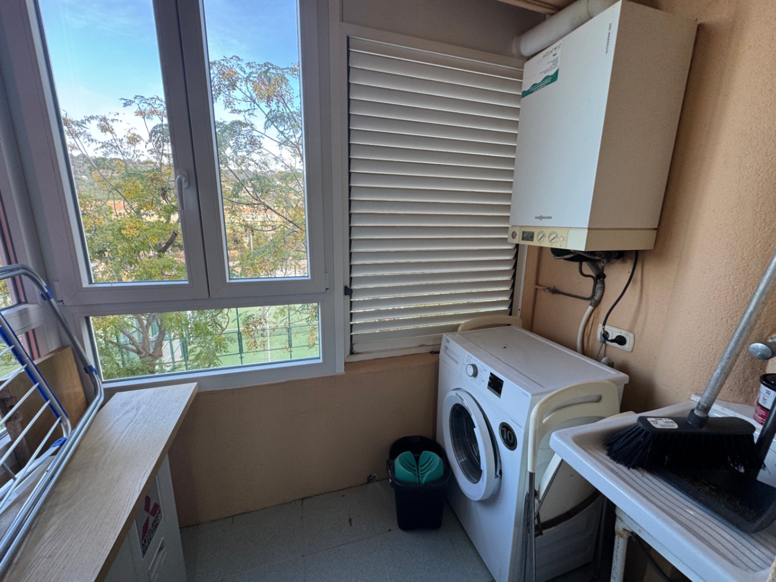 Functional utility room featuring a front-load washing machine, gas boiler, and sink. Large windows provide ample natural light and views of the outdoor greenery.