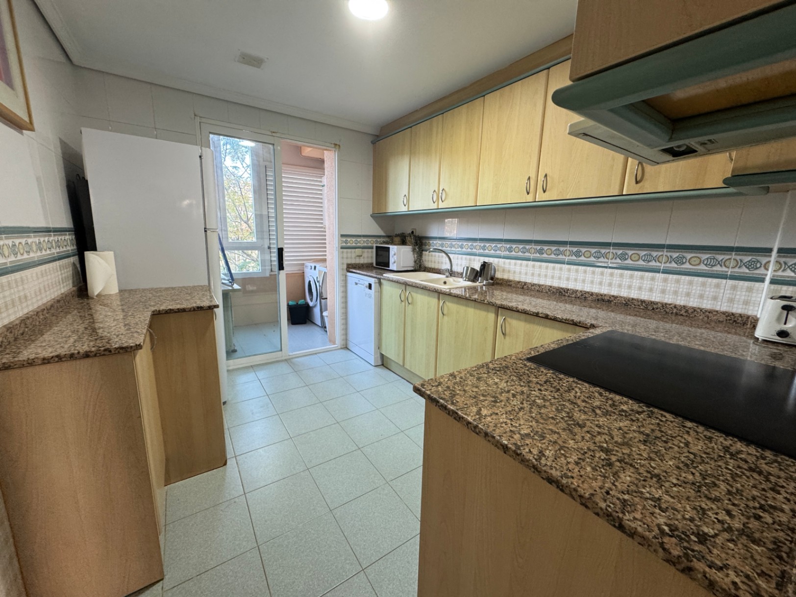 Kitchen with light wood cabinetry, granite countertops, and white appliances. A sliding glass door leads to a utility balcony with a washing machine.