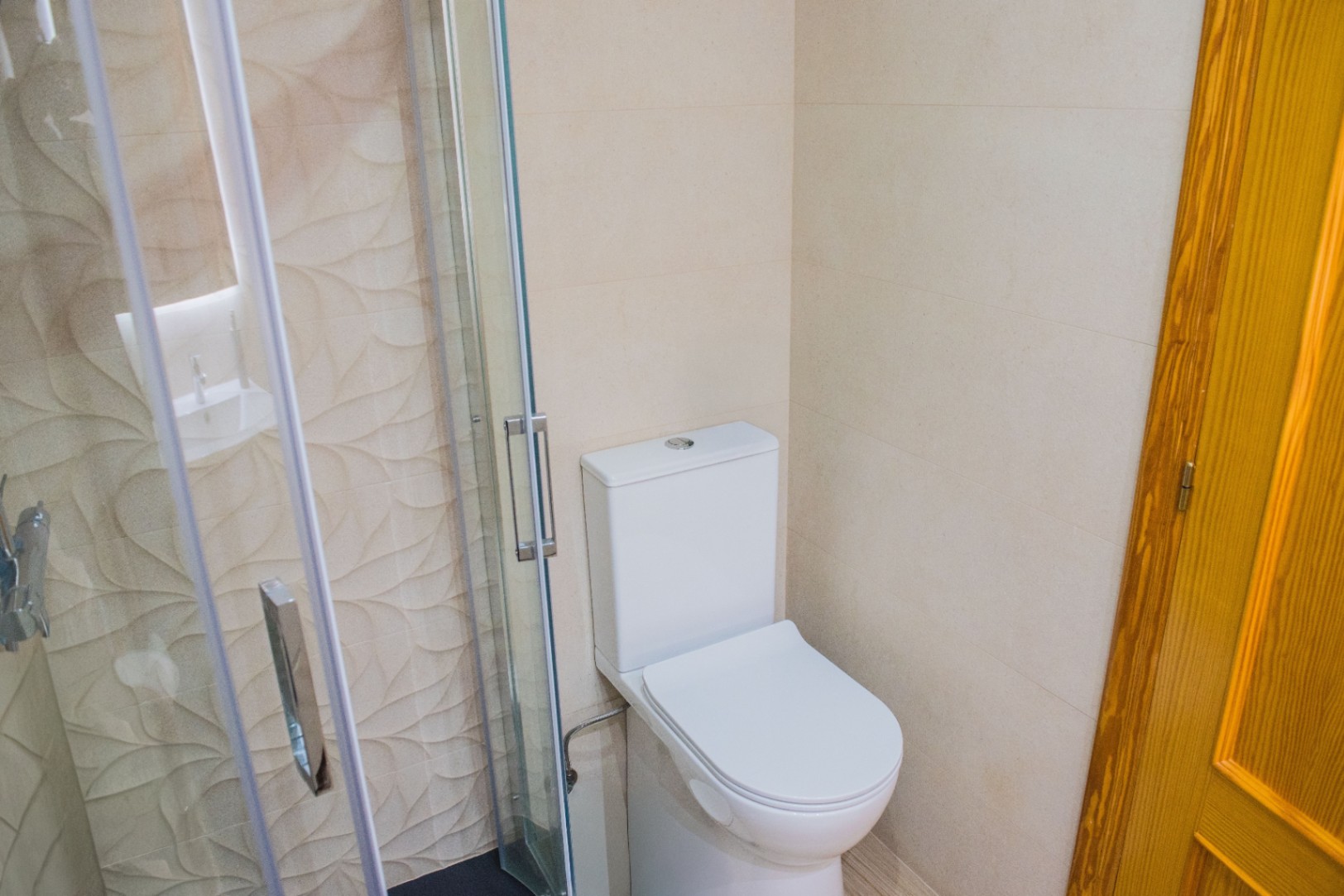 Bathroom corner featuring a white toilet alongside a glass shower cabin with textured decorative tiling and chrome fixtures.