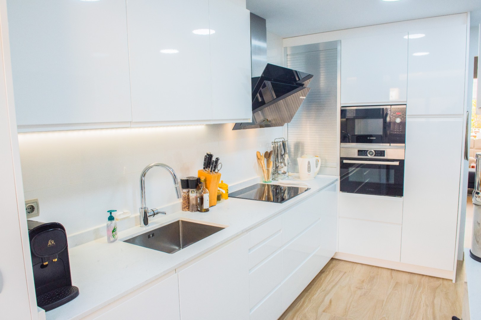Modern kitchen featuring white high-gloss cabinetry, integrated Bosch appliances, and a sleek induction cooktop with an angled extractor hood over a white quartz countertop.