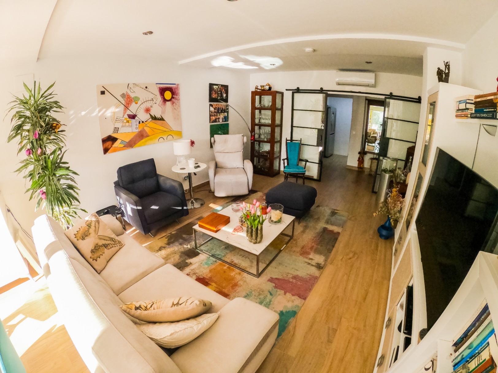 Modern living room featuring a white sectional sofa, colorful abstract art, and a marble coffee table on a vibrant rug. Industrial-style sliding glass doors lead to the adjacent rooms.